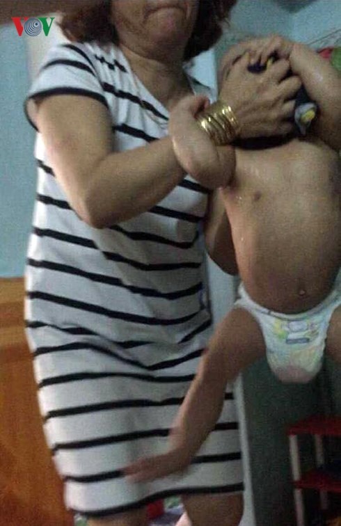 Bà Hồng dùng hai tay xách một bé trai ra khỏi cũi.