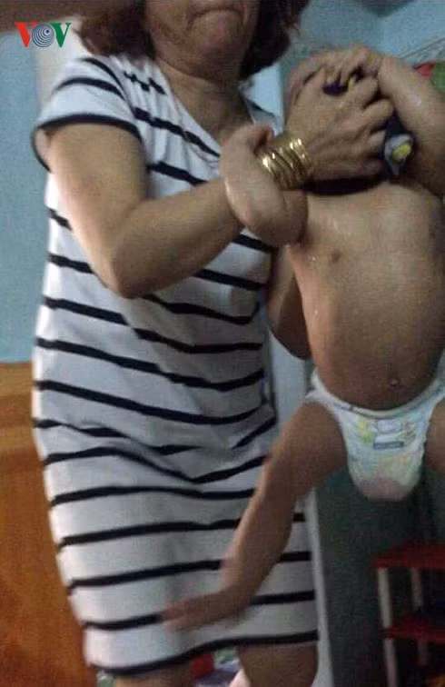 Bà Hồng dùng hai tay xách một bé trai ra khỏi cũi.