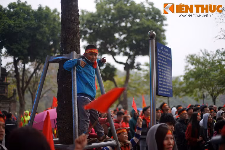 Một cậu bé trèo lên giá đỡ của cây xanh để xem trận đấu qua màn hình trước Bưu điện Hà Nội.