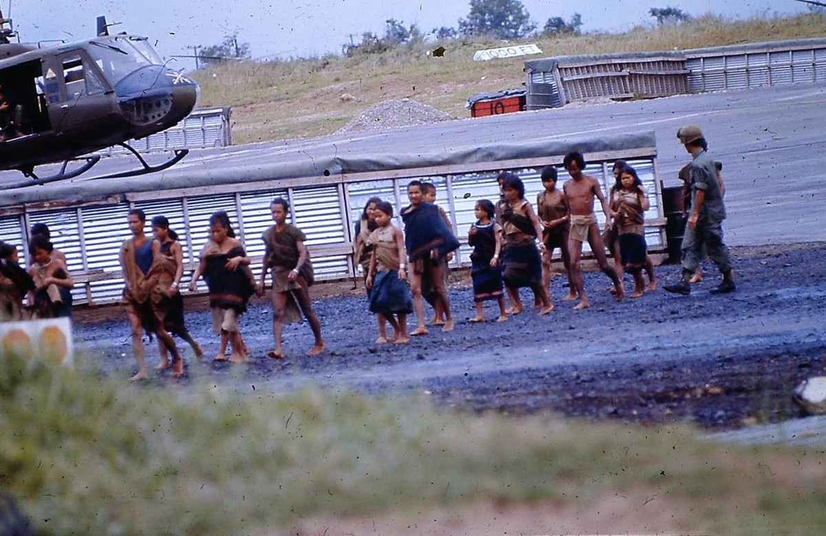 Một nhóm cư dân người Thượng đi qua sân bay Cheo Reo khi được di dời khỏi vùng oanh kích tự do. Đây là khu vực được bảo vệ đặc biệt quanh sân bay, nơi quân đội Mỹ có thể khai hỏa vào bất cứ đối tượng khả nghi nào mà không cần sự cho phép từ sở chỉ huy. Ảnh: 203rdhawkeyes.net.