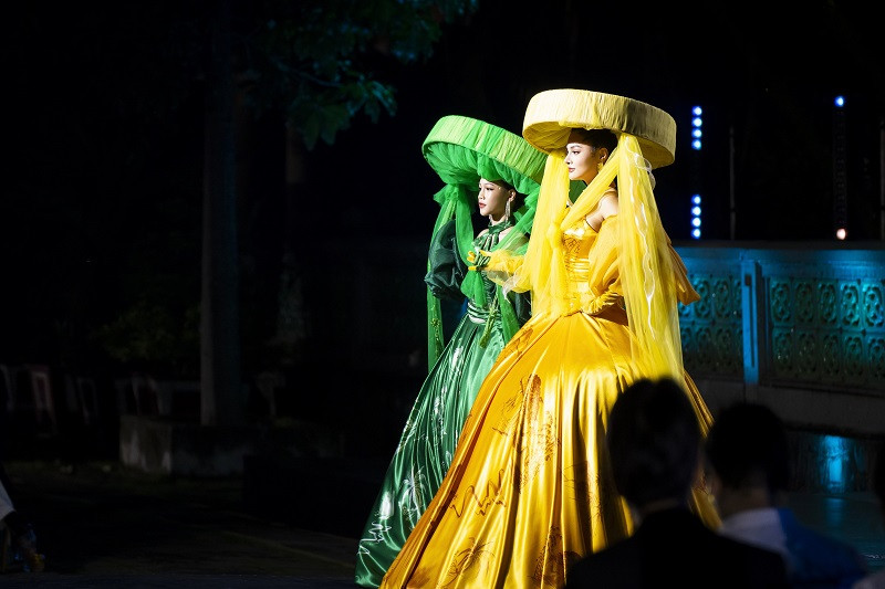 Hai màu xanh - vàng quyện hòa với nhau, tôn thêm vẻ đẹp của tà áo dài lấy cảm hứng từ chiếc yếm đào, sử dụng công nghệ in ấn tranh 3D khắc họa khung cảnh làng quê, núi non Việt Nam hùng vĩ. Bức tranh giang sơn càng trở nên lấp lánh với hàng ngàn viên pha lê được đính kết thủ công tỉ mỉ, tinh xảo. Bên cạnh đó, chiếc nón thúng quai thao cách điệu cũng tạo thêm nét thú vị, sống động cho hai người mẫu diễn kết màn.