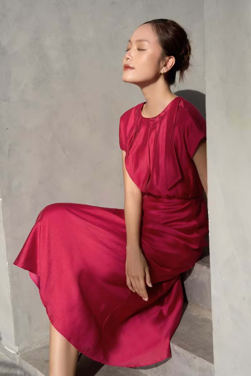 Đầm dáng xòe nhẹ cùng chiều dài midi, được thiết kế theo phong cách cổ điển, tinh tế nhưng vẫn đủ nổi bật qua các điểm nhấn xếp nếp phần chân cổ và thân trước.