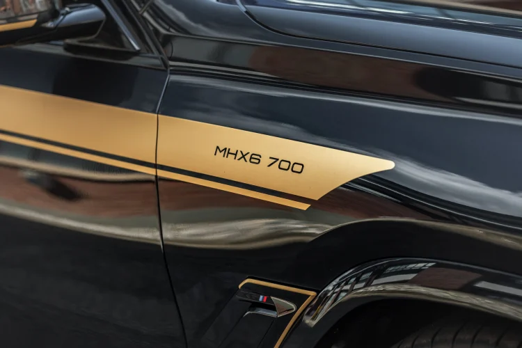 Manhart cũng sử dụng sợi carbon cho nắp gương, cửa gió bên phía sau và các chi tiết sau xe. Bộ decal của Manhart là thứ giúp người khác dễ dàng nhận ra nhất với màu đen bóng cùng các điểm nhấn sọc màu vàng đồng.