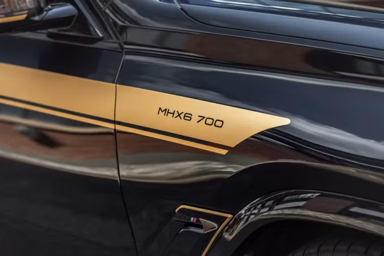 Manhart cũng sử dụng sợi carbon cho nắp gương, cửa gió bên phía sau và các chi tiết sau xe. Bộ decal của Manhart là thứ giúp người khác dễ dàng nhận ra nhất với màu đen bóng cùng các điểm nhấn sọc màu vàng đồng.