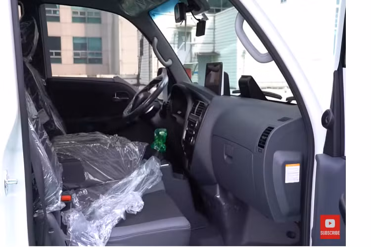 Khi nhìn vào bên trong cabin, ta thấy chiếc Bongo 3 EV này vẫn còn mới nguyên. Nó vẫn còn lớp ni-lông bọc ghế, vô lăng, và nhiều thứ khác. Cabin xe không được sang trọng lắm, phù hợp với một chiếc xe phục vụ công việc nặng nhọc, nhưng nó cũng có một vài trang bị công nghệ hiện đại như hệ thống thông tin giải trí màn hình cảm ứng.