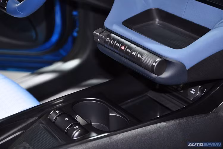 Nằm ngay phía dưới màn hình này là khay đựng đồ nhỏ và một dãy núm xoay chỉnh các tính năng của xe, bao gồm cả chuyển số. Dưới nữa là 2 hộc đựng cốc, 3 núm xoay chỉnh một số tính năng an toàn của xe và sạc điện thoại thông minh không dây.