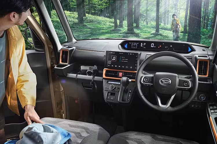 Chưa hết, Daihatsu Tanto FunCross 2023 còn được trang bị ghế bọc nỉ màu rằn ri, lưng ghế sau và sàn khoang hành lý chống thấm nước. Trước mặt người lái xuất hiện vô lăng 3 chấu, tích hợp phím chức năng và bảng đồng hồ kỹ thuật số khá dài, nằm cao trên mặt táp-lô. Bên cạnh đó là màn hình thông tin giải trí dạng cảm ứng 9 inch và cụm điều khiển trung tâm đặt khá cao.