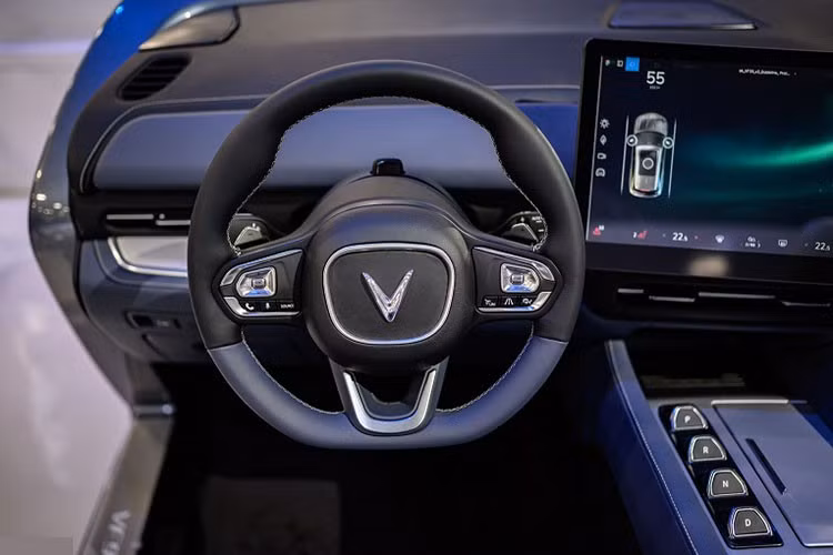 Cụm đồng hồ thông số truyền thống phía sau vô-lăng cũng được lược giản, tích hợp vào màn hình giải trí trung tâm. Vô-lăng của Vinfast VF9 tạo hình chữ nhật bo tròn bốn góc cá tính, tích hợp các phím chức năng hỗ trợ lái tiện lợi. Thiết kế này khá sát với bản concept trước đó, cần số dạng nút bấm thời thượng.