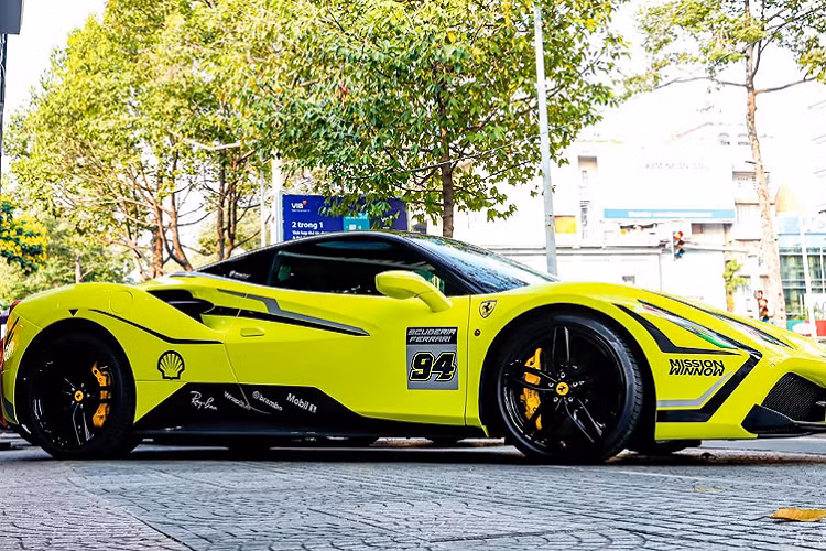 Đặc biệt, phần đèn pha còn được dán decal một phần để mang đến cái nhìn sắc sảo và táo bạo hơn. Nhiều vị trí trên xe xuất hiện số 94. Nhìn tổng thể, Ferrari 488 GTB vô cùng ấn tượng nhờ màu sơn “phát sáng” cùng bộ tem đua bắt mắt.