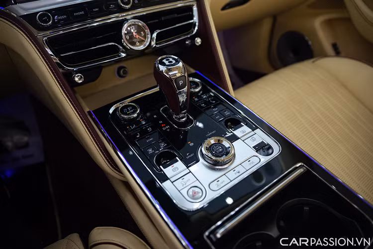 Bước vào bên trong, nội thất Bentley Flying Spur sang trọng với tông màu đỏ/be, kết hợp với các chi tiết bằng da, gỗ và kim loại màu bạc. Bảng táp-lô được ốp gỗ Piano Black. Vô lăng 3 chấu bọc da đồng màu nội thất tích hợp nhiều nút bấm hỗ trợ người lái.