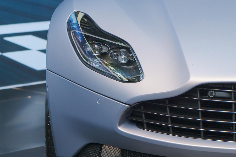 Điểm nhấn ở phần đầu xe vẫn là lưới tản nhiệt với 5 nan ngang và 10 nan dọc tối màu. Phần nắp ca-pô thiết kế hình vỏ sò đi kèm với 2 khe gió lớn (phiên bản V12 có 4 khe). Chiếc Aston Martin DB11 V8 trang bị bộ mâm đa chấu kép phay xước 2 tông màu tương phản, kết hợp với cùm phanh màu vàng phía sau.