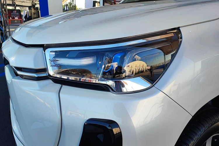 Tại đây, Toyota Hilux phiên bản thuần điện gần như bị bịt kín lưới tản nhiệt vì không cần làm mát khoang động cơ. Ở chính giữa đầu xe là khe gió nhỏ, tích hợp logo của hãng Toyota và 2 nẹp mạ crôm vắt ngang, kéo dài đến đèn pha. Bên dưới là 4 khe gió hẹp hơn rồi mới đến hốc gió trung tâm hình thang.