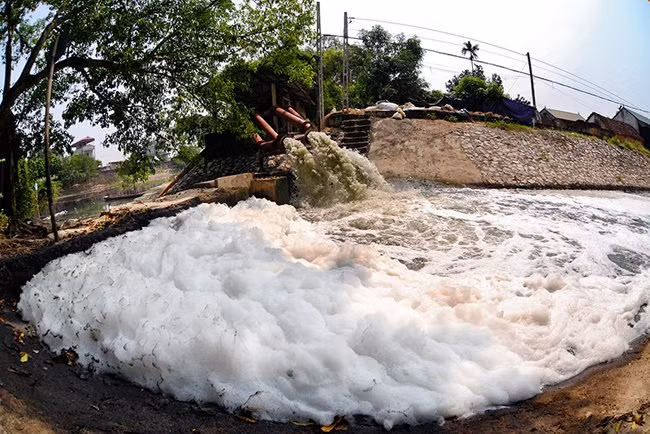 Nước từ sông Nhuệ được bơm vào một kênh thủy lợi ở xã Mỹ Hưng (Thanh Oai, Hà Nội). Dòng nước sủi bọt trắng xóa bốc mùi hôi thối nồng nặc này vẫn được người dân hàng ngày sử dụng để tưới tiêu trong đồng ruộng.
