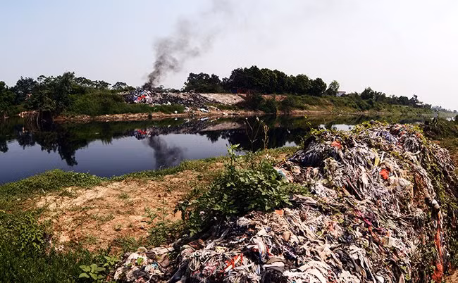 Vải vụn chất thành đống dọc bên bờ sông và xử lý bằng cách đốt tạo nên bầu không khí khét lẹt nồng nặc. Số tàn tro của vải vụn sau khi đốt được vứt thẳng xuống dòng sông vốn đã đen kịt và đặc quánh bởi chất thải.