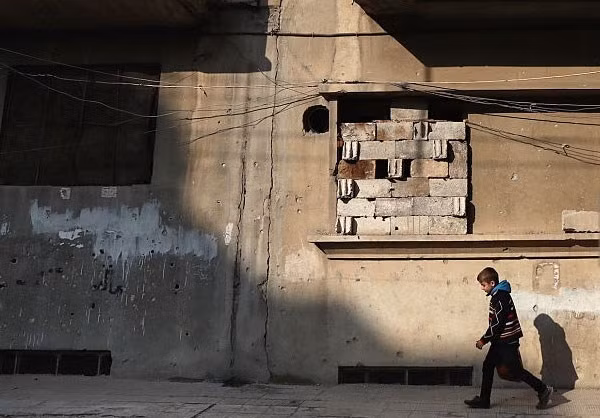 Một bé trai đi bộ trên đường phố Aleppo.