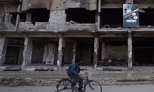 Người đàn ông đạp xe qua những tòa nhà đổ nát trong chiến tranh ở Aleppo.