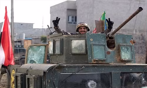 Một binh sĩ Iraq giơ biểu tượng chiến thắng khi đứng trên xe quân sự.