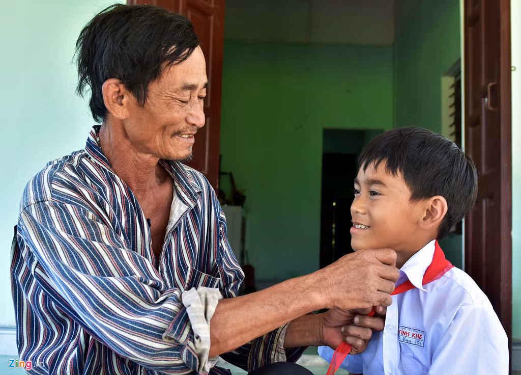 Ông Ba trò vừa đeo khăn quàng vừa trò chuyện vui vẻ cùng con trai trước giờ đến trường. Ảnh: Minh Hoàng.