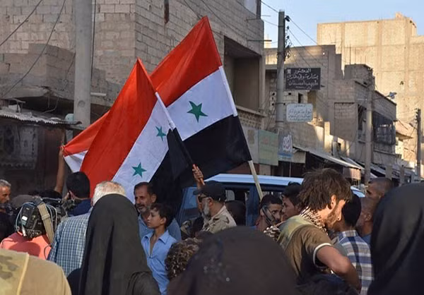 Người dân cầm lá cờ Syria trên một con phố đông đúc. Ảnh: FNA.