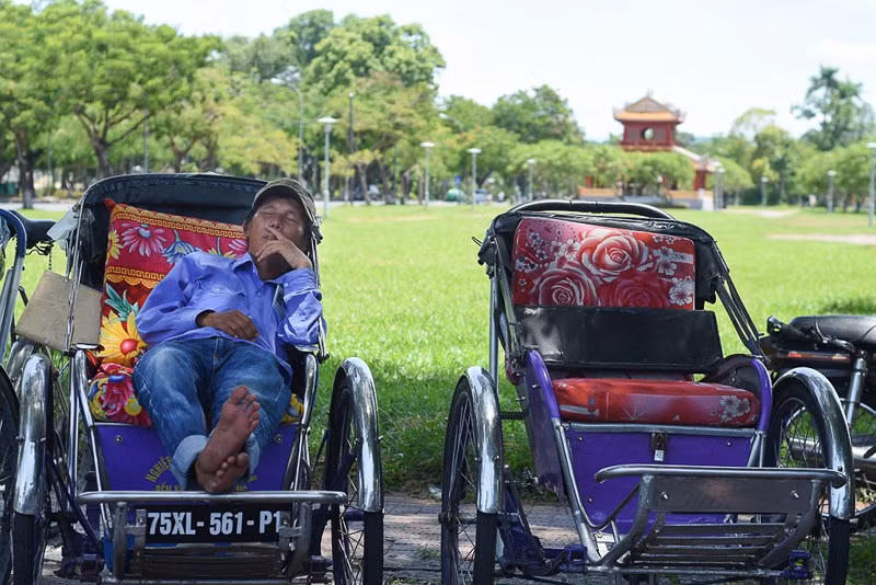 Người đạp xích lô tranh thủ giấc ngủ trưa dưới bóng râm ở bờ Bắc sông Hương. Ảnh: NGUYỄN DO