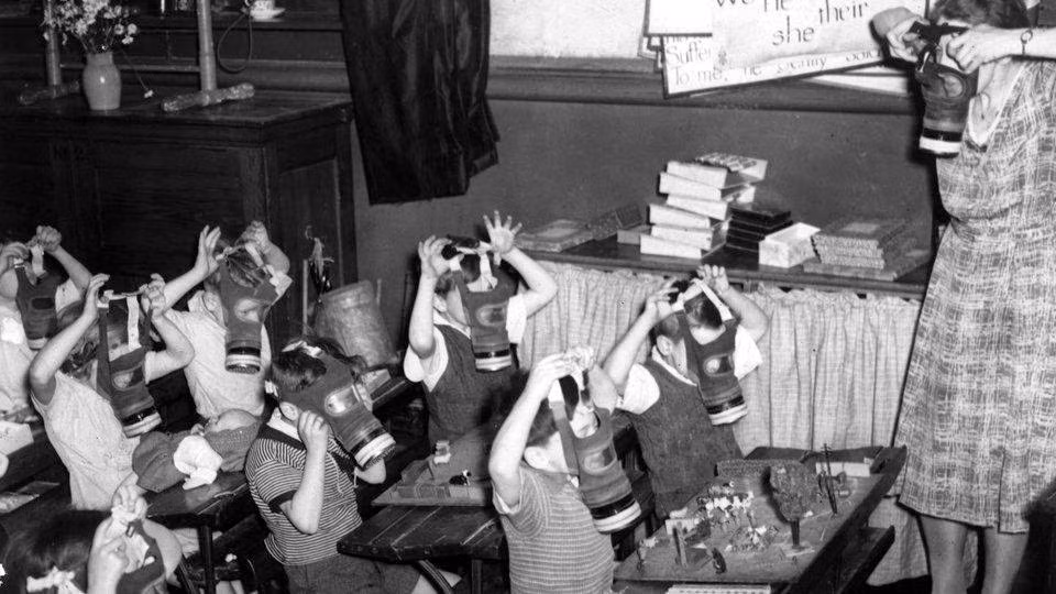 Một lớp học của trẻ em Anh ở hầm ngầm trú ẩn dưới lòng đất ở vùng nông thôn khi Đức quốc xã không kích các thành phố lớn của nước này. Nữ giáo viên dạy học sinh cách sử dụng mặt nạ phòng độc đề phòng trường hợp bị kẻ thù tấn công bằng vũ khí nguy hiểm này.