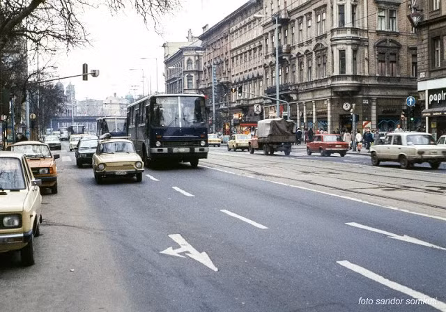 Đường phố Budapest đông đúc xe cộ. Hai bên đường là những tòa nhà văn phòng, cửa hàng tấp nập người đi lại.