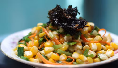 Cho đầu hành vào xào tiếp, giảm lửa rồi cho ngô vào xào chung. Ngô chín thì cho hành lá, nêm nếm gia vị vừa miệng rồi tắt bếp. Trút bắp xào ra dĩa và cho rong biển khô lên trên. Món ăn ngon hơn khi còn nóng. Ảnh: tin247