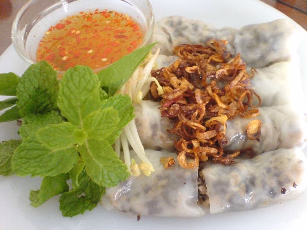 Bánh cuốn vỉa hè Nguyễn Bình Khiêm (đoạn cắt Trần Nhân Tông). Phục vụ buổi tối. Quán bánh cuốn hút khách bởi chất lượng bánh rất ngon, tráng mỏng tang và hành phi tự nhà làm, không phải hành phi công nghiệp. Ngoài món bánh cuốn ra, cửa hàng còn phục vụ chân gà, trứng hấp. Nếu bạn ra vào tầm 7-8h tối thì sẽ phải ngồi đợi rất lâu đấy nhé. Ảnh: wordpress.com.