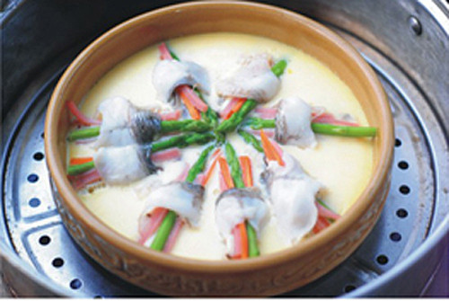 Cá thái lát mỏng, uớp với rượu trắng, muối, dầu ăn, đường và một ít gừng đá thái sợi. Trứng gà đạp ra bát, đánh đều tay. Cho cá vào đĩa sâu lòng rồi rưới đều lòng trứng đã đánh tan lên trên. Sau đó, cho cá vào nồi hấp hấp khoảng 10 phút. Cá chín thì rác ngò gai thái nhỏ và một chút bột tiêu vào cho món ăn dậy mùi thơm. Ảnh: trithuctre