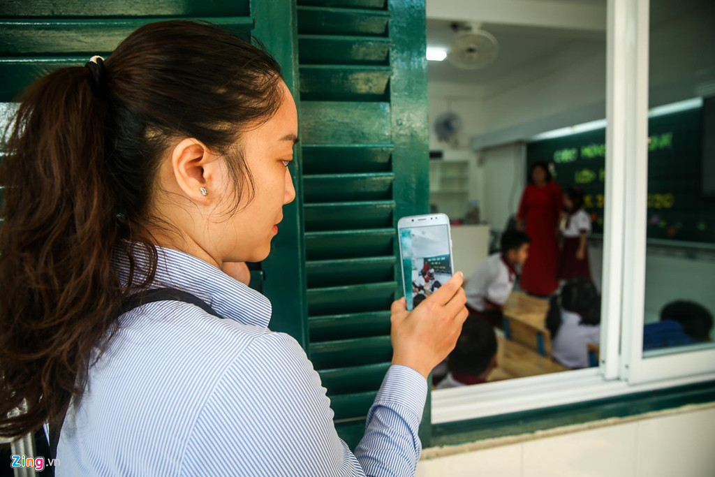 Phụ huynh nán lại, ghi nhận khoảnh khắc ngày đầu con đi học từ cửa sổ lớp học. Để tạo kỷ niệm đẹp và không khí tươi vui cho con trẻ trong ngày đầu đi học, nhiều gia đình huy động tất cả thành viên cùng đưa con đi học lớp 1. Con gái đã vào lớp nhưng vợ chồng anh Khánh cùng con gái lớn vẫn nán lại, cổ vũ bé từ bên ngoài. “Bé rất vui, hào hứng, vừa đến lớp đã làm quen được bạn cùng bàn. Nhưng lần đầu tiên đi học mà, mình muốn để lại kỷ niệm vui nên cả gia đình cùng đến trường với con”, anh Khánh chia sẻ.