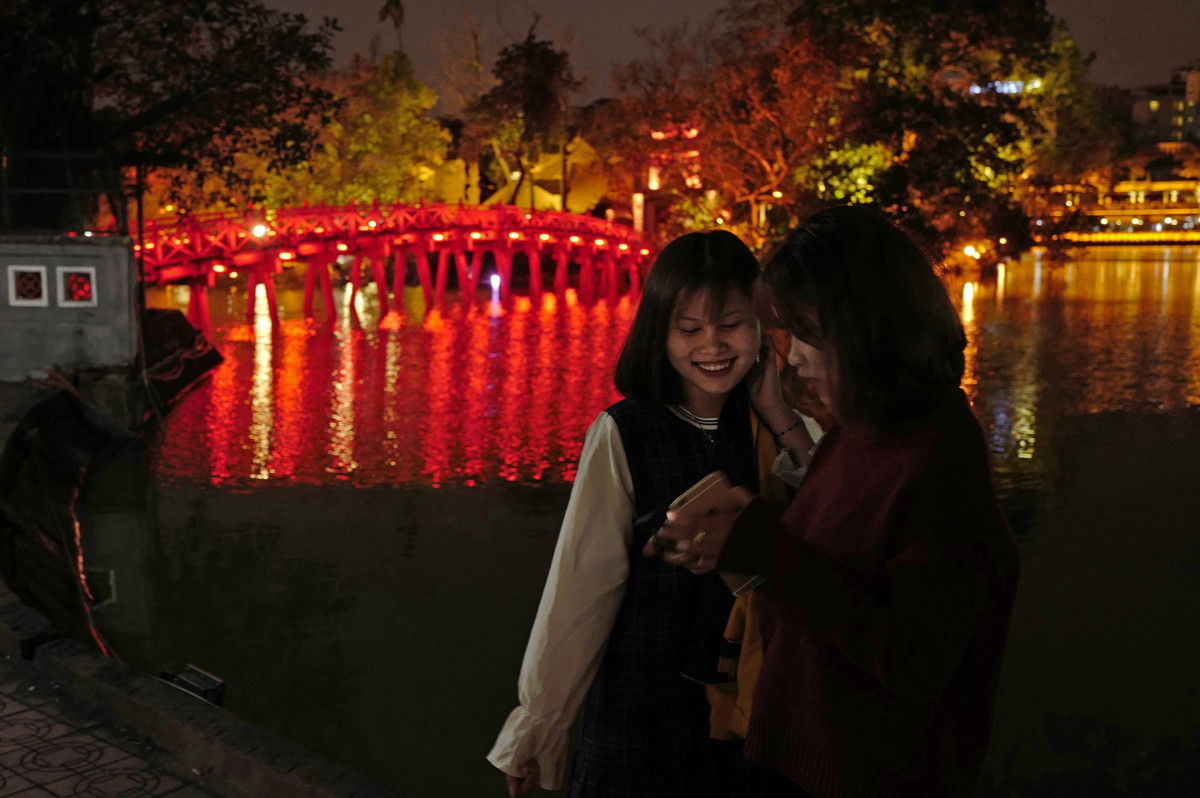 Hai cô gái trẻ xem lại ảnh họ vừa chụp trên điện thoại di động, bên cạnh cầu Thê Húc dẫn ra đền Ngọc Sơn - di tích quốc gia đặc biệt của Việt Nam, một trong những biểu tượng của Thủ đô Hà Nội.