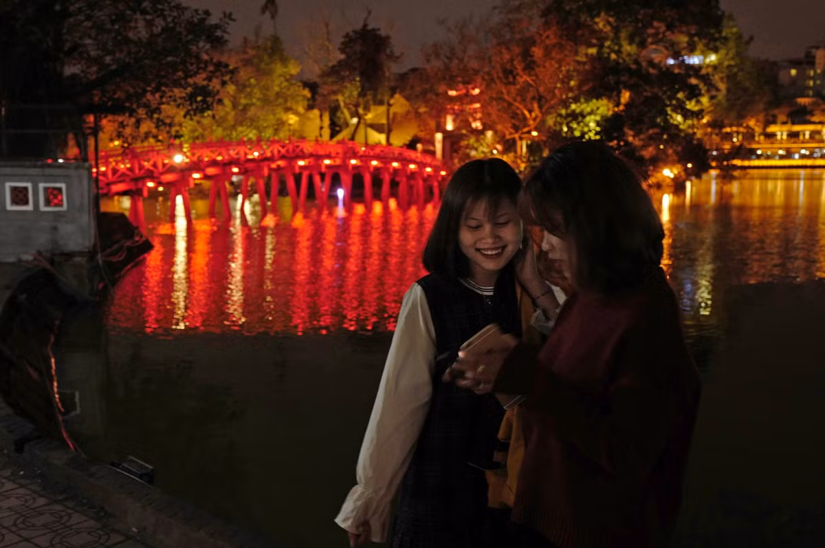 Hai cô gái trẻ xem lại ảnh họ vừa chụp trên điện thoại di động, bên cạnh cầu Thê Húc dẫn ra đền Ngọc Sơn - di tích quốc gia đặc biệt của Việt Nam, một trong những biểu tượng của Thủ đô Hà Nội.