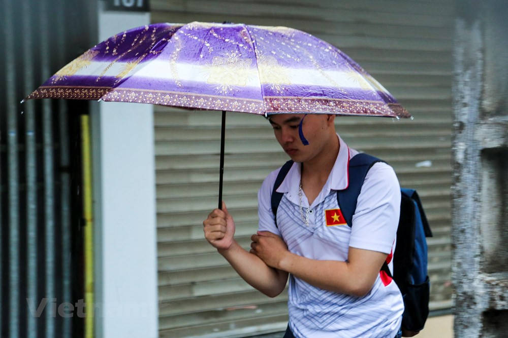 Nhiều người vẫn chủ quan mặc áo cộc ra đường đã phải co người lại vì không khí lạnh kèm theo mưa rào. (Ảnh: Minh Sơn/Vietnam+)