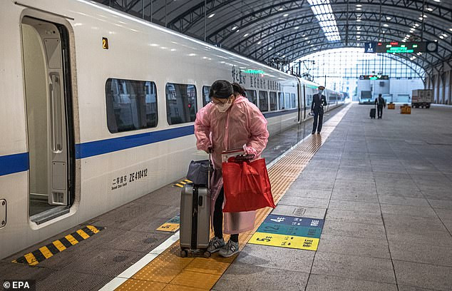 Người phụ nữ đeo khẩu trang và mặc bảo hộ cẩn thận mang theo hành lý đứng gần chuyến tàu chính thức đầu tiên rời Vũ Hán sau khi lệnh phong tỏa được dỡ bỏ. Ảnh: EPA.