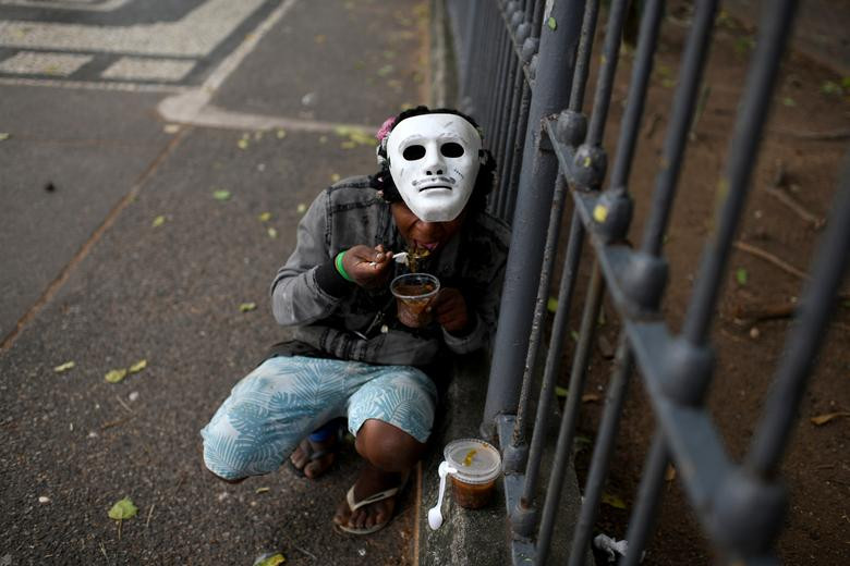 Một người vô gia cư ngồi ăn ngoài đường phố ở Rio de Janeiro, Brazil, hôm 11/4.