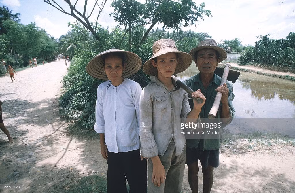 Một cậu bé có mẹ là người Việt, bố là lính Mỹ đứng giữa cha mẹ nuôi ở Cần Thơ năm 1985.