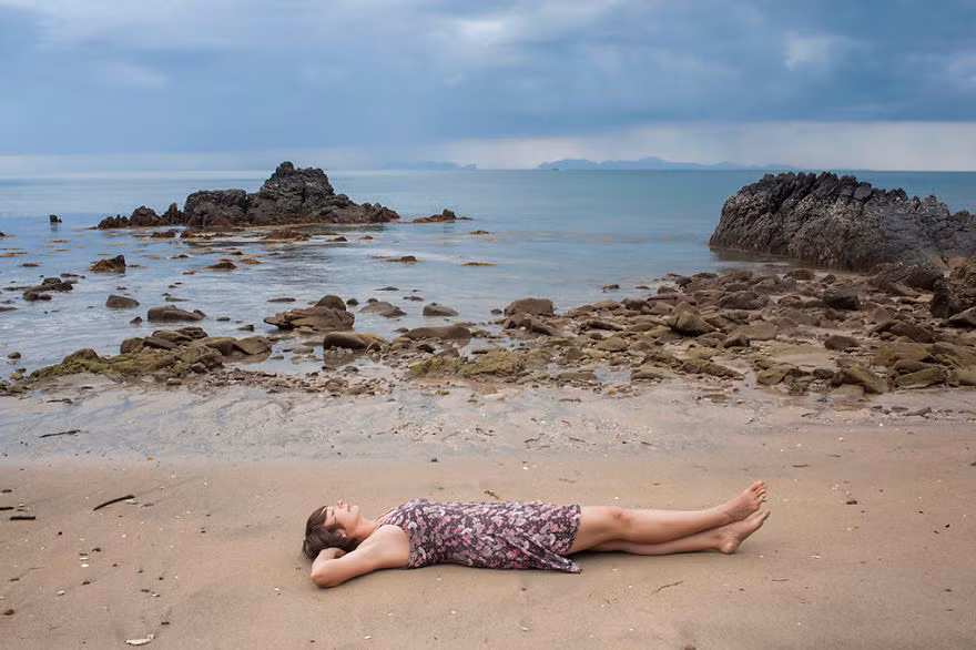 Hình ảnh nữ nhiếp ảnh nằm trên bãi biển hoang vu, măc chiếc váy xòe mềm mại, dáng vẻ rất thư thái, ung dung.