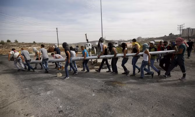 Những người biểu tình Palestine khiêng một chiếc cột để chặn đường trong cuộc đụng độ với binh sĩ Israel gần khu định cư Do thái Bet El, gần thành phố Ramallah, Bờ Tây ngày 13/10.