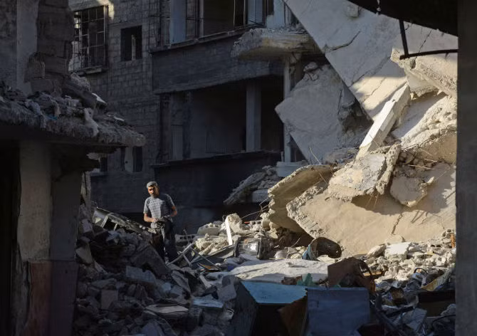 Một người dân địa phương trên đống đổ nát giữa những tòa nhà bị phá hủy trong khu vực Dahane ở thủ đô Damascus.