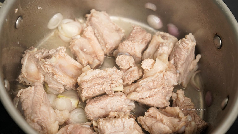 Bước 3: Lấy một cái nồi khác, đổ một lượng dầu thích hợp, cho hành băm nhỏ và gừng thái sợi vào phi thơm, đổ sườn đã chần vào, quấy đều một lúc trên lửa nhỏ. Khi thịt trên bề mặt sườn vàng đều thì đổ một lượng rượu nấu ăn thích hợp vào trộn đều để khử mùi tanh hiệu quả. (Ảnh: cookbeo)