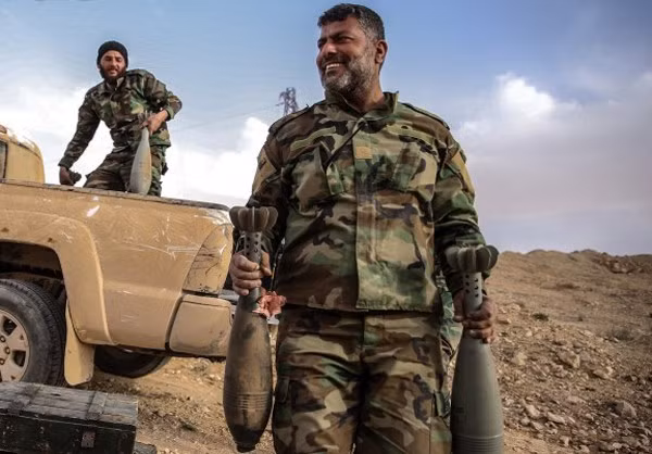 Các binh sĩ Syria cười tươi vận chuyển những quả đạn cối cỡ lớn xuống mặt đất.