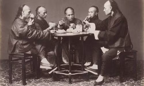 Những người đàn ông trong trang phục truyền thống, tóc tết đuôi sam cùng nhau ăn cơm.