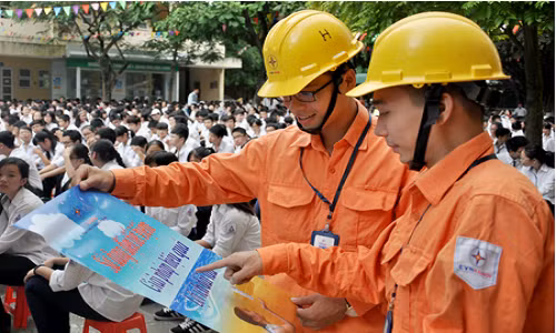 Tuyên truyền viên Công ty Điện lực Ba Đình phát tờ rơi, dán poster tuyên truyền tiết kiệm điện tại trường THPT Phạm Hồng Thái - Ảnh: Hoa Việt Cường.