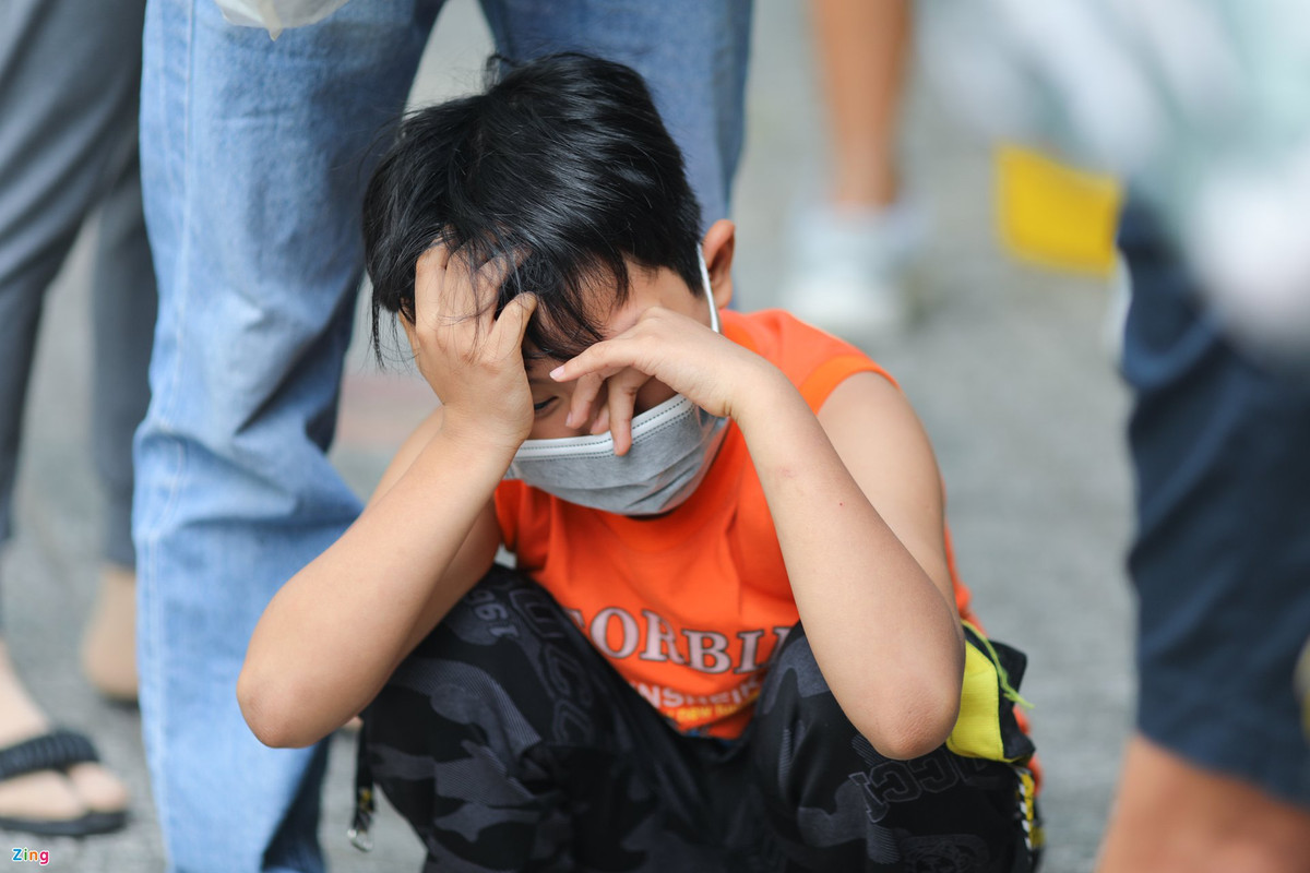 Bé Anh Hào (10 tuổi) ngồi bệt trong lúc xếp hàng chờ. Phụ huynh bé Hào cho biết một ngày trước, bé có biểu hiện sốt cao nhưng test nhanh tại nhà vẫn âm tính. Đến sáng nay, gia đình đưa bé lên bệnh viện xét nghiệm thì kết quả dương tính. Do lượng trẻ tại bệnh viện quá đông, 2 cha con phải chờ gần 2 tiếng mà chưa tới lượt khám sàng lọc.