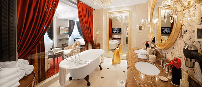 Phòng tắm được trang trí với tông màu chủ đạo là vàng và đỏ, lãng mạn, có bồn tắm đứng kiểu Pháp và tắm xông hơi. Không gian sáng, lấp lánh nhờ gương, đèn chùm, tường kính lớn. Giá phòng Tổng thống hiện là 4.851 USD (hơn 107 triệu đồng). Ảnh: Internet.