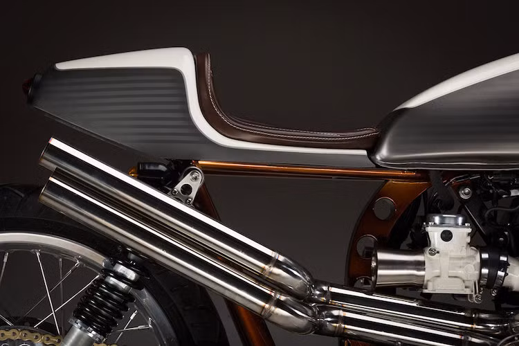 Cặp ống xả được bẻ góc theo đường xéo dưới đuôi xe. Chiếc yên da mỏng với các đường chỉ đều một cách hoàn hảo do hãng Beyond Trim làm riêng cho Rumour Monger.