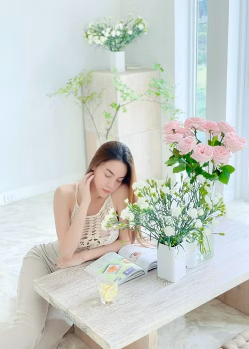 Nữ ca sĩ đọc sách thư giãn trong không gian ngập tràn hoa, cây xanh.