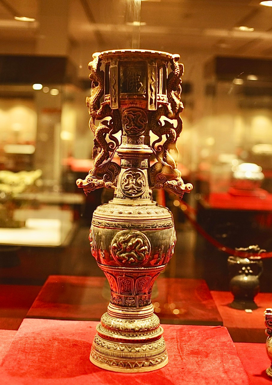 Chân đèn gốm, men lam xám, thớt trên cổ đèn trang trí hai tượng rồng hai bên và đắp nổi rồng ổ. Thân đèn vai đắp nổi cánh sen và nhũ hoa, giữa than đắp nổi rồng ổ. Chân đèn đắp nổi nhiều tầng hoa. Niên đại thế kỷ 16.