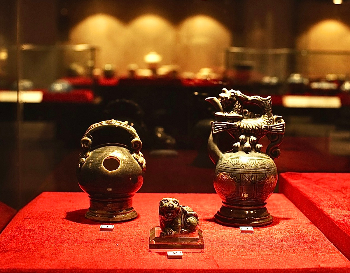 Từ trái sang: Bình vôi gốm quai đắp nổi thạch sùng. Tượng hổ. Ấm gốm quai hình cá hóa long. Cả ba đều bằng gốm có men lam xám.