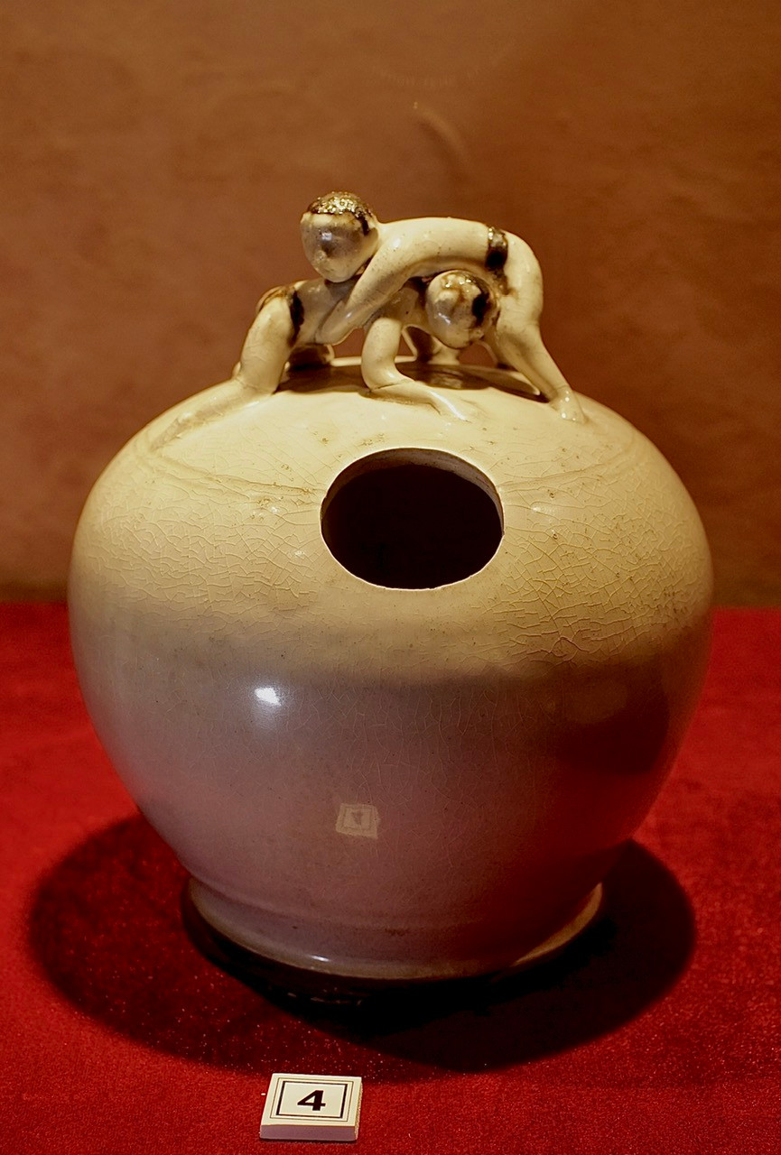 Bình vôi gốm, men trắng ngà, quai tượng người đấu vật, có niên đại thế kỷ 14-15.